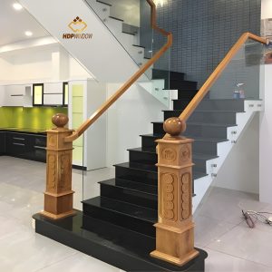 Mẫu cầu thang kính tay vịn gỗ sồi kết hợp trụ gỗ lớn (trụ cái) vững chãi.