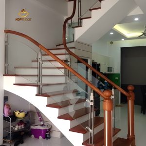 Mẫu cầu thang kính tay vịn gỗ tròn, trụ gỗ và bậc đá có cùng tông màu.